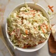 A bowl of coleslaw made with shredded cabbage, carrots, and green onions, coated in a creamy dressing.