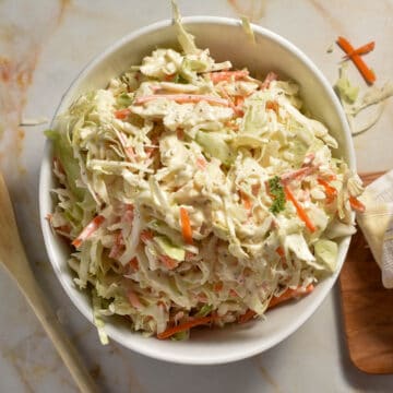 A bowl of coleslaw made with shredded cabbage, carrots, and green onions, coated in a creamy dressing.