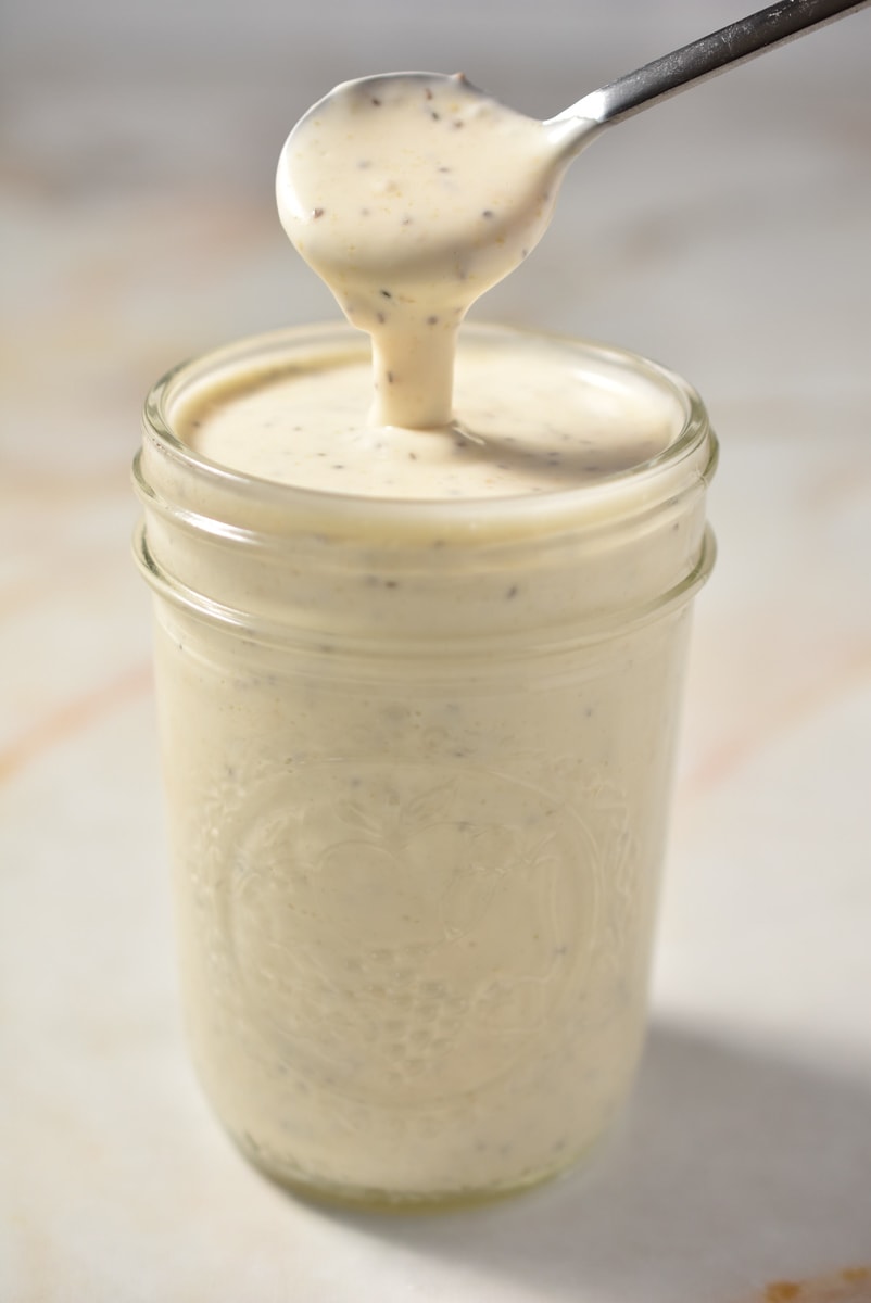 A mason jar filled with creamy coleslaw sauce, accompanied by a spoon.