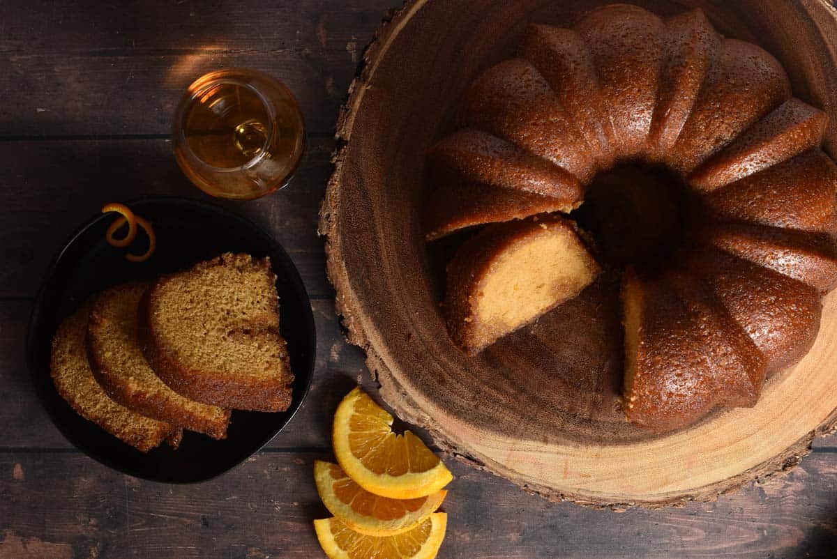 glazed bundt cake on a wooden platter and three slices on a plate with orange garnish. 