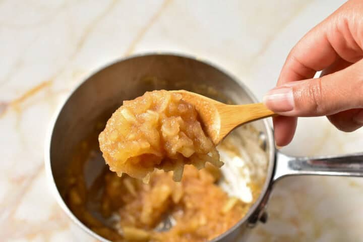 a wooden spoon with apple filling scooped out of the pan.