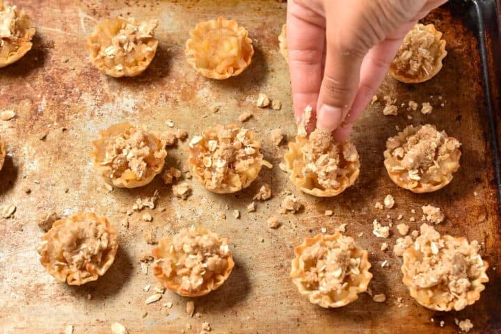hand sprinkling crumble topping onto apple cups.