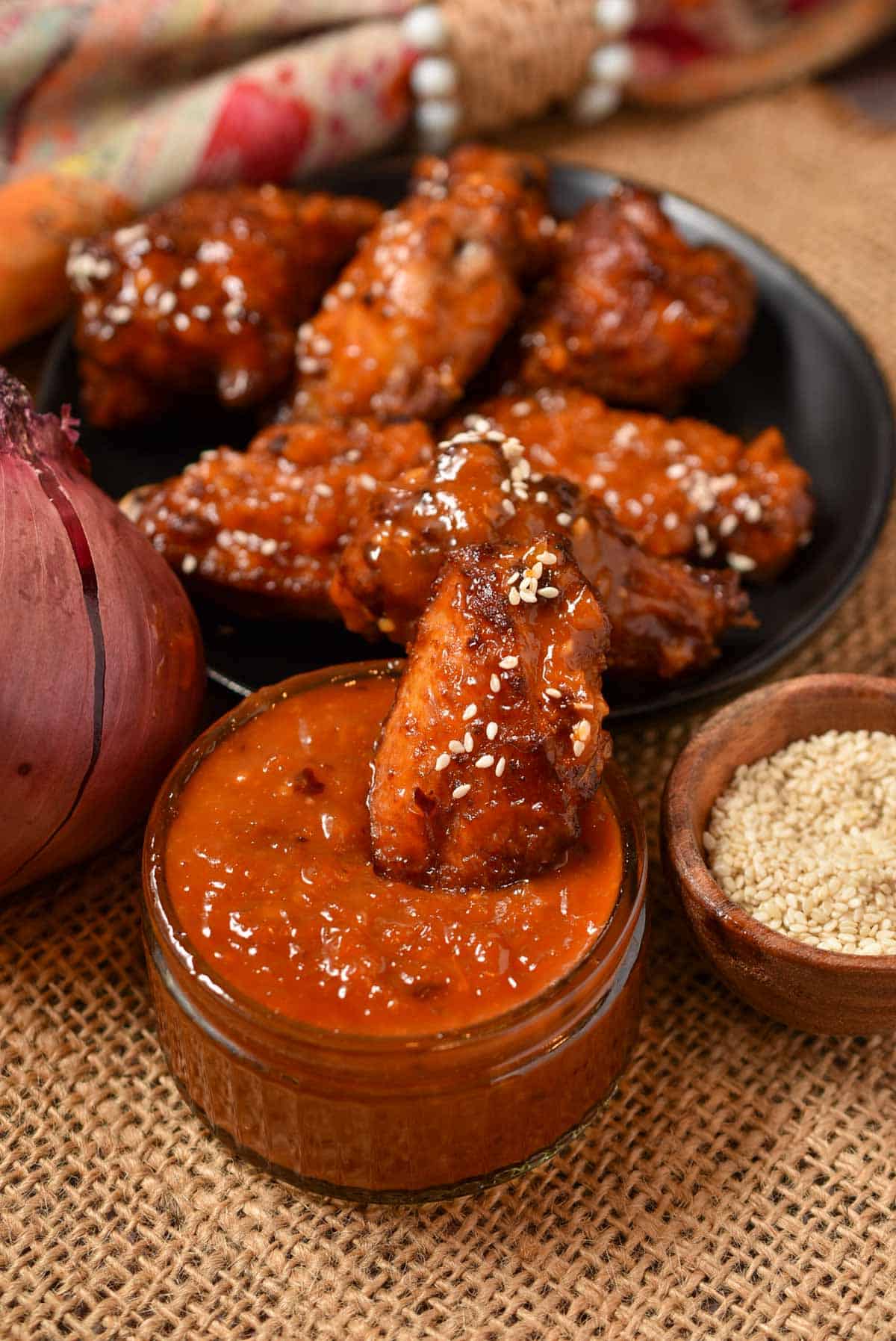chicken wing sitting in a bowl of Asian zing sauce with sesame seeds.