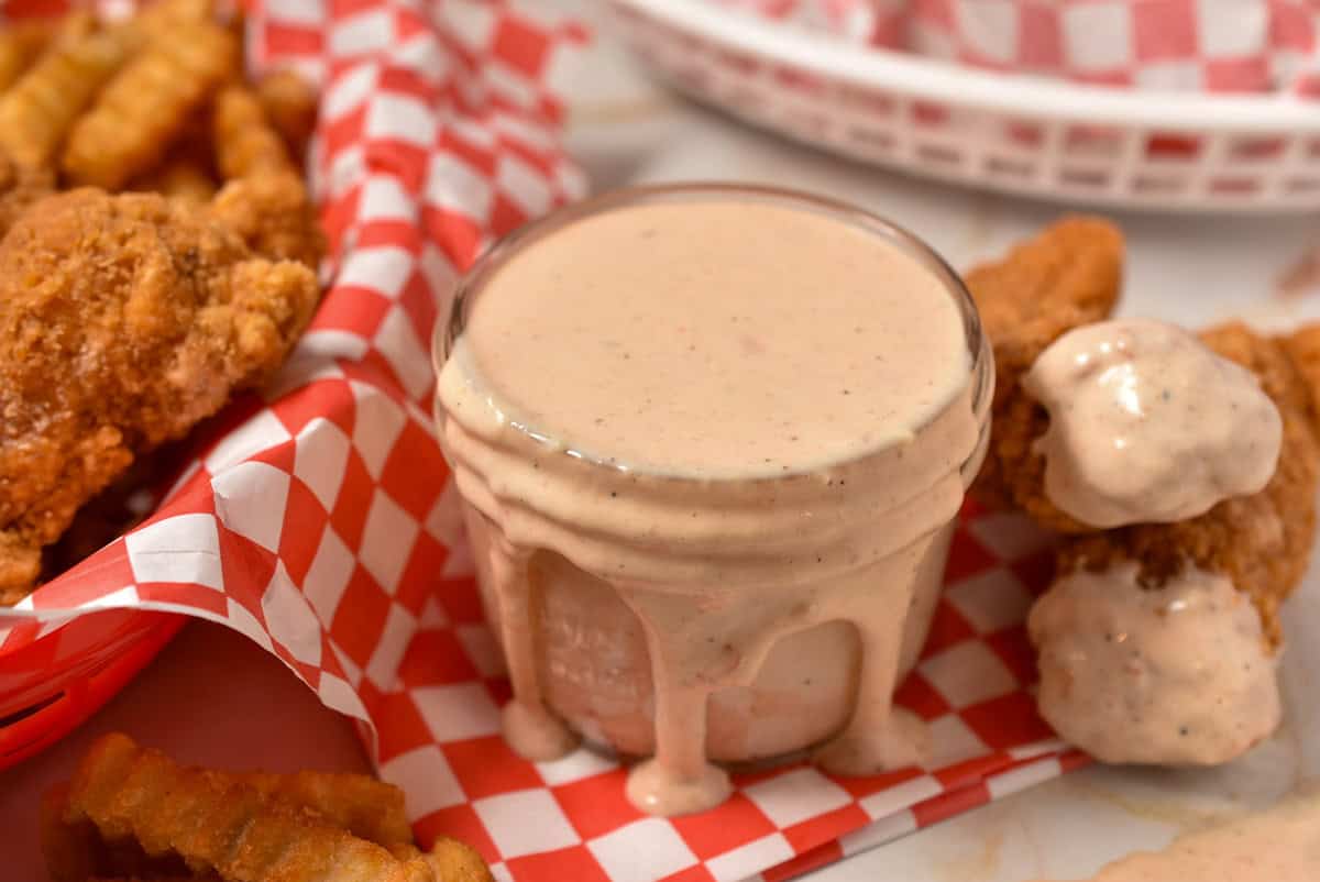chicken tenders dipped into sauce that is overflowing from a glass bowl.