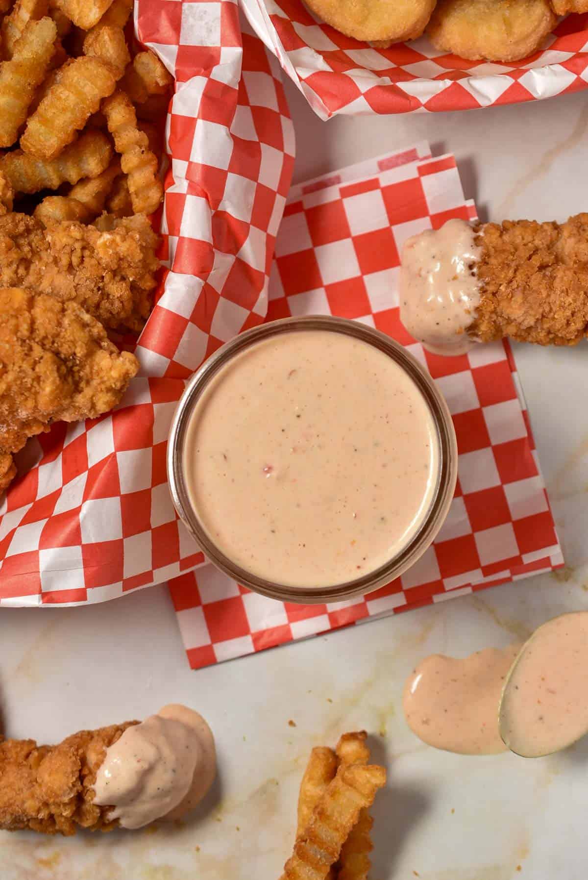 bo sauce in a glass bowl sitting on a checkered paper with French fries and chicken tenders.