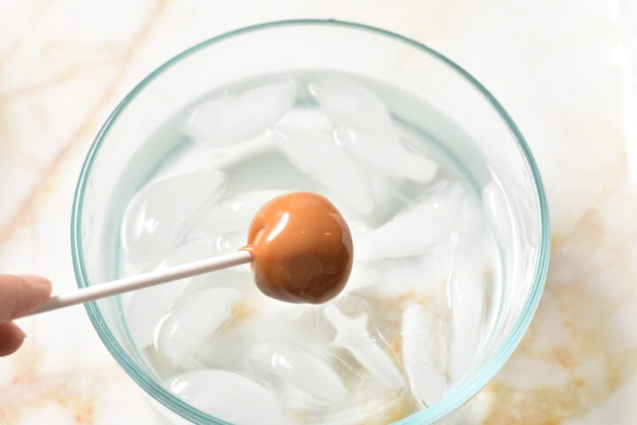 caramel coated apple on a stick, waiting to be dipped in a bowl of ice water.