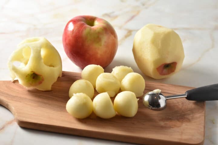 small balls of apple cut with a melon baller sitting on a cutting board.