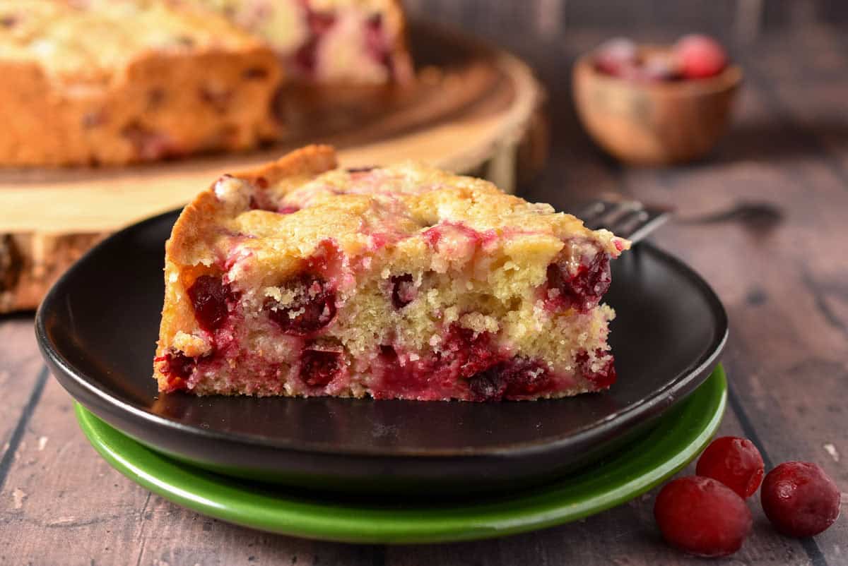 cranberry cake on plate with a fork and cranberry garnish.