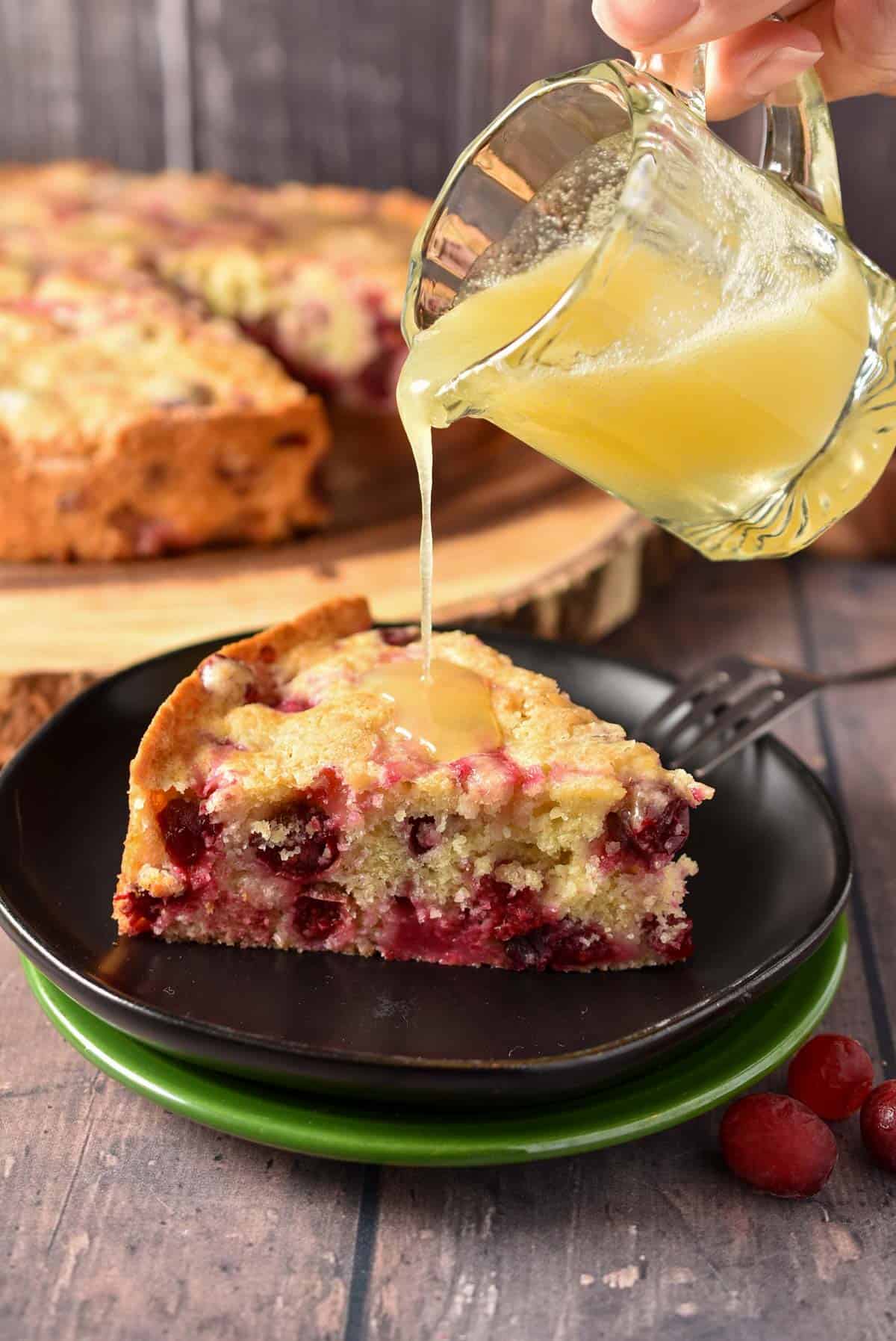 cranberry cake with butter sauce being poured over the top.