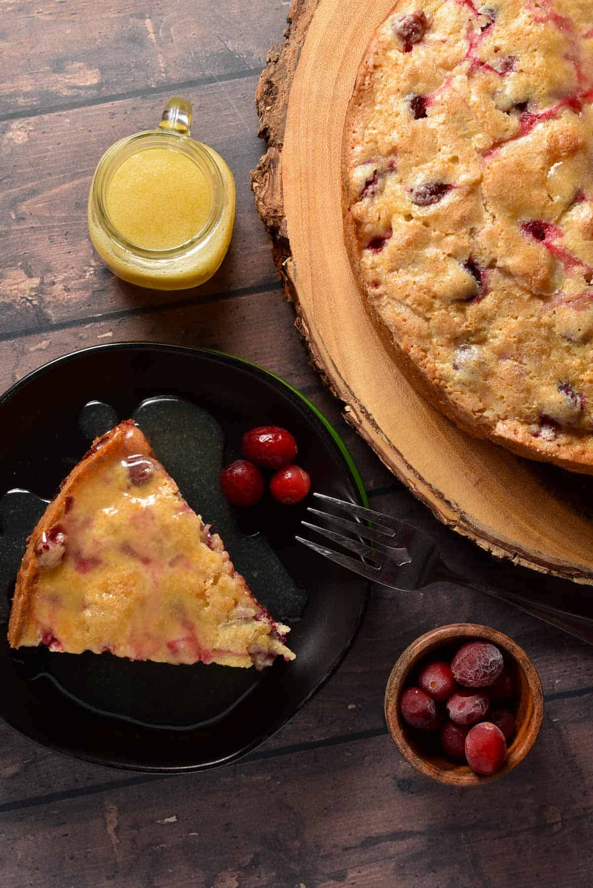 cranberry cake slice with butter sauce in a mini pitcher on a wooden board.