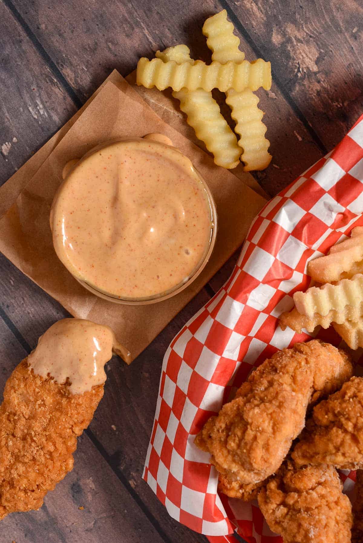 Close-up of a crunchy chicken strip coated in smooth, creamy Sonic Signature Sauce with french fries.