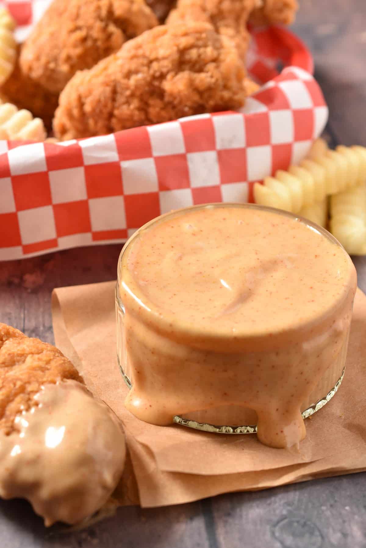A golden, breaded chicken tender covered in thick Sonic Signature Sauce, with a bowl in the background.