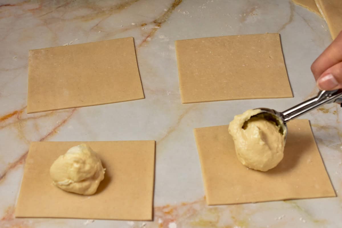 Pie filling being scooped into pie crusts on the counter.