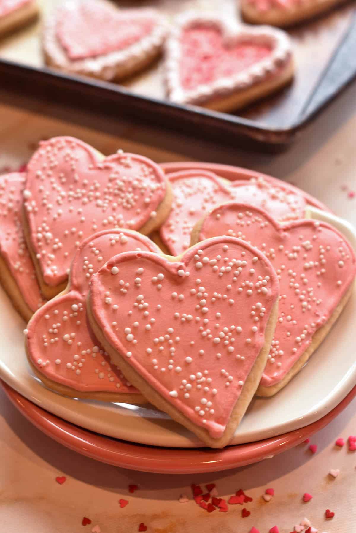 A plate of heart sugar cookies, each adorned with thick royal icing and vibrant sprinkles for a festive touch.