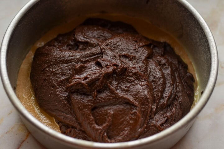 Cake batter with a layer, poured into a round baking pan, on top of parchment paper.