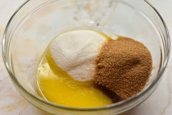 A glass bowl holds melted butter, white sugar, and brown sugar.