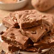 A stack of chocolate fudge pieces with pecans on a plate, with whole potatoes in the background, showcases this old-fashioned Potato Fudge recipe—a classic potato dessert thats rich and decadent.