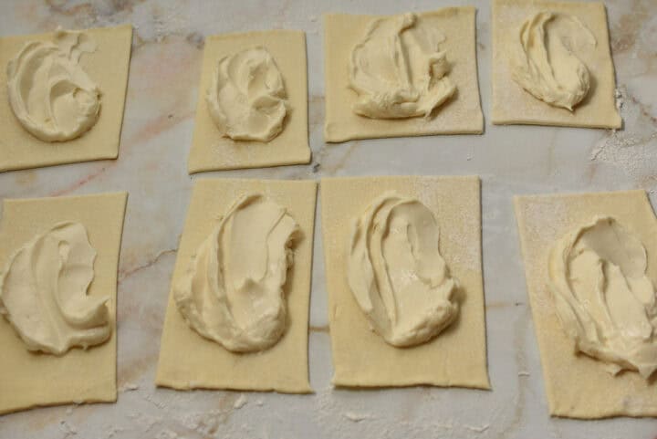 Eight rectangular pieces of dough, reminiscent of a Cheese Danish from Starbucks, are topped with a dollop of cream cheese filling and arranged on a floured surface, ready for baking.