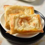 Two rectangular pieces of golden-brown puff pastry, reminiscent of a Starbucks Cheese Danish, with a slightly crumpled surface, are placed on a small white plate.