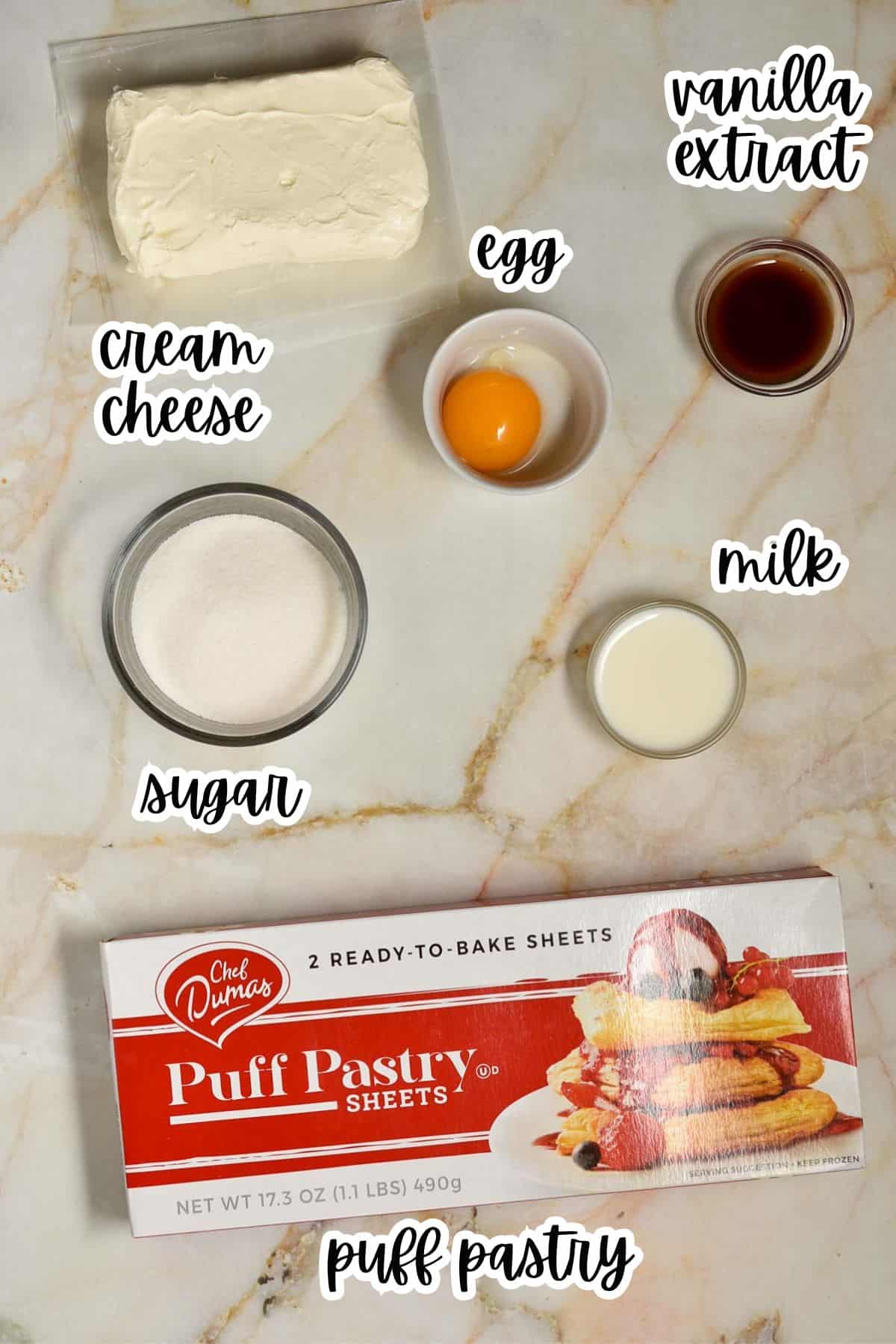 A top view of ingredients for a recipe inspired by Starbucks Cheese Danish: cream cheese, sugar, a cracked egg, milk, vanilla extract, and a box of puff pastry sheets on a marble surface.