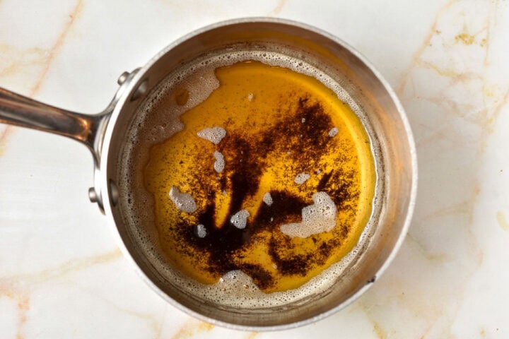A saucepan containing melted browned butter with visible brown specks on the surface, perfect for adding rich flavor to your Gingerbread House Bundt Cake, placed on a light-colored countertop.