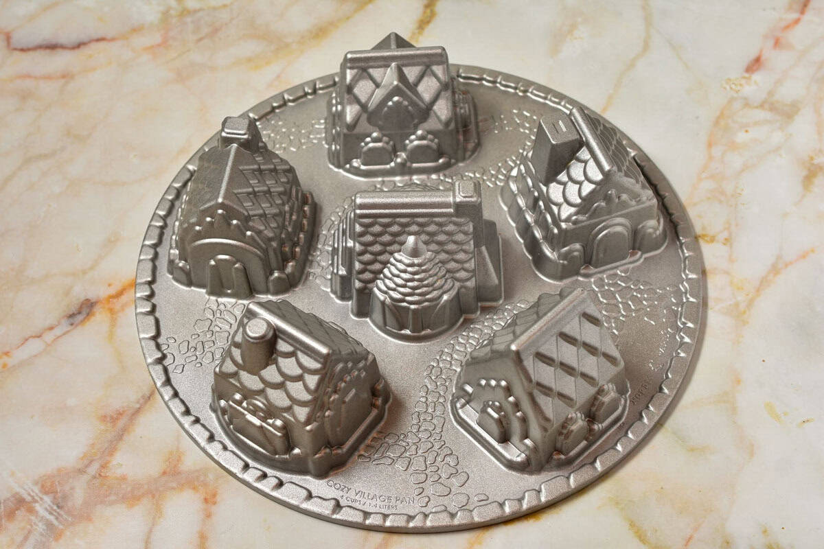 Round metal baking pan with six molds shaped like small houses, perfect for creating charming Gingerbread House Bundt Cake treats, placed on a marble surface.