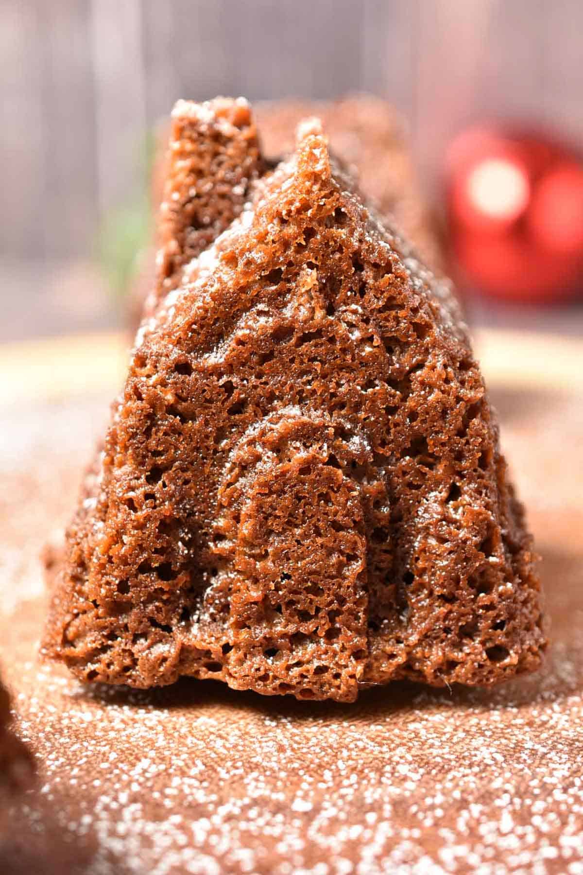 A Gingerbread House Bundt Cake, dusted with powdered sugar, sits on a wooden surface, its charming shape resembling a small house or church.
