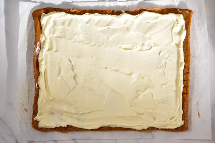 A rectangular sheet cake with a layer of white frosting spread evenly on top, placed on parchment paper-perfect as a Thanksgiving make-ahead dessert.