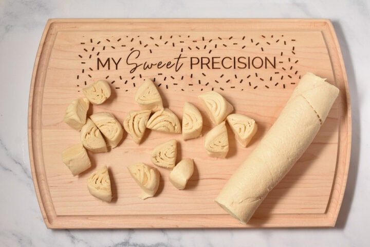 Unbaked rolled dough cut into pieces on a wooden cutting board engraved with