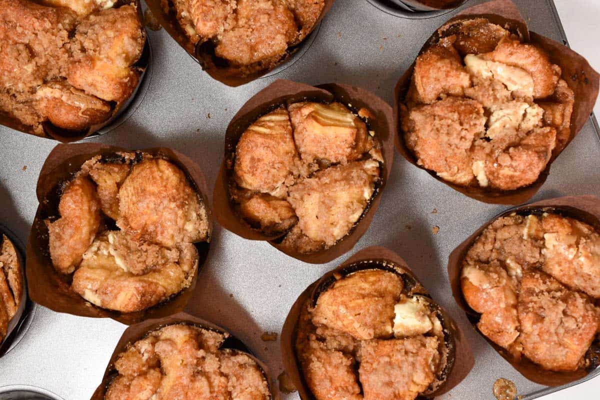 Top-down view of several muffins with a crumbly brown cinnamon topping in a metal muffin tin, reminiscent of Starbucks Copycat Cinnamon Pull-Apart Bread.