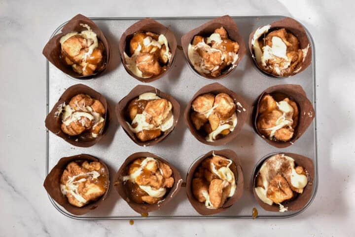 A muffin tin with twelve sections, each holding a paper liner filled with baked Starbucks Copycat Cinnamon Pull-Apart Bread pieces drizzled with icing.